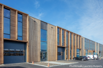 Modern Blueprint Automation (PBA) gebouw in houtstijl met meerdere grote ramen en garagedeuren. Auto’s staan geparkeerd ervoor, met een blauwe lucht op de achtergrond.