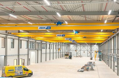 Een industriële hal met meerdere loopkranen op een baan, op de voorgrond een ABUS-servicevoertuig.