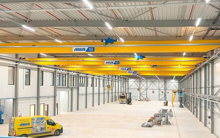 Een industriële hal met meerdere loopkranen op een baan, op de voorgrond een ABUS-servicevoertuig.