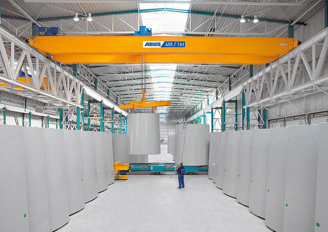 Een loopkraan verplaatst zware lasten in een industriële hal, terwijl een medewerker in de werkruimte staat.