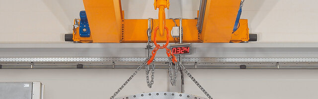 Loopwerkdrager met opzetstukken van een kraan, waaraan een kettinghanger met last is bevestigd.