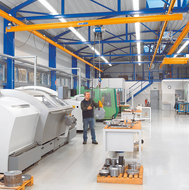 Een medewerker bedient een hangbaansysteem met kettingtakel en verplaatst een last in een fabriekshal