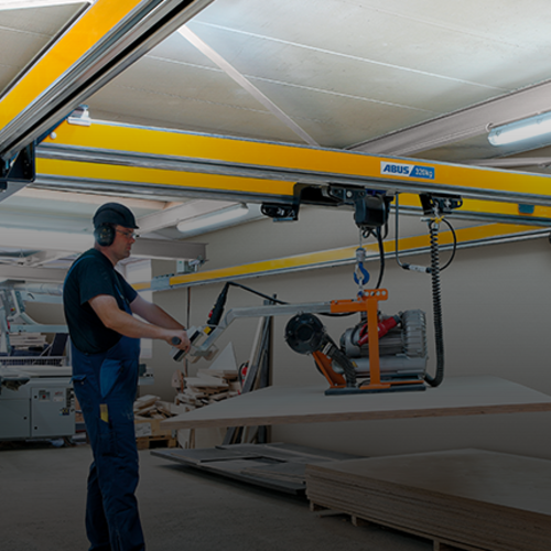 Een medewerker bedient een dubbelligger-loopkraan van het type ZHB-X en hijst een last met een kettingtakel in een fabriekshal.